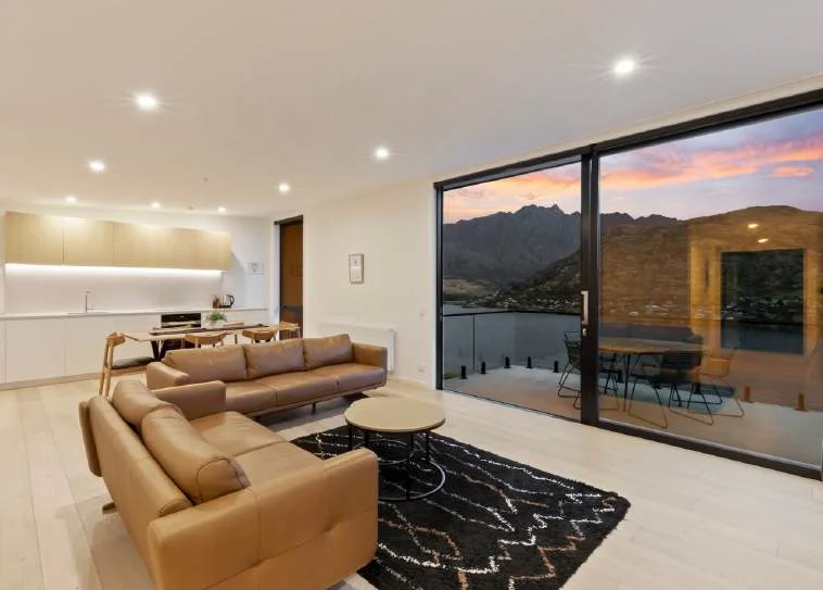 Furnished open-plan living room opening to a balcony with Lake Wakatipu and mountain views